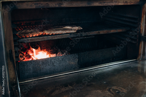 the cook prepares juicy meat steaks in a large oven on a charcoal grill