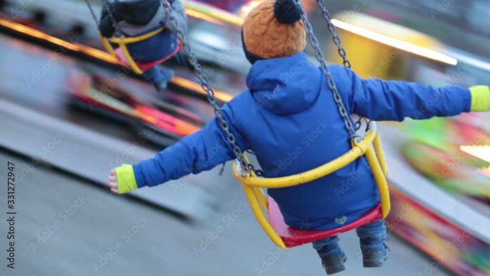 Child, cute boy riding chain swing carousel on sunset, motion blur, colorful background