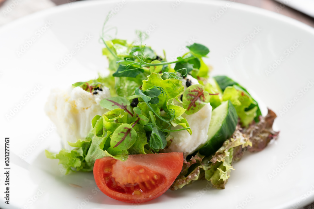 Light diet salad of mozzarella and fresh vegetables -cucumber, tomato, lettuce, peas on a white plate on a wooden background Light diet salad of mozzarella and fresh vegetables -cucumber, tomato, lettuce, peas on a white plate on a wooden background