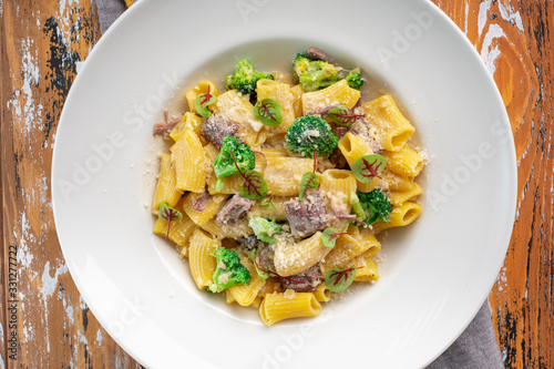 Rigatoni pasta with beef on a white plate with Parmesan and steamed broccoli