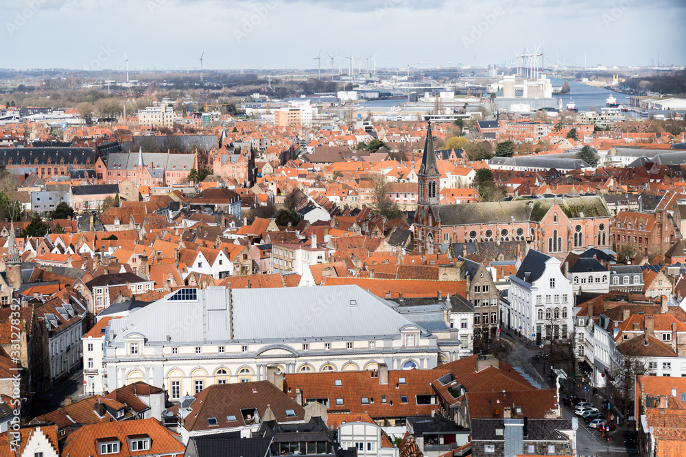 Panoramic view of Old Town in Bruges, Belgium. Red roofs, trees and quiet streets below. Photo taken through fence net.