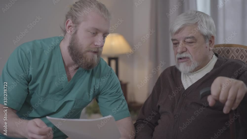 Close-up of Caucasian male nurse explaining matter of documents to mature retiree. Man assisting senior in nursing home. Help, support, aging, lifestyle. Close-up of Caucasian male nurse explaining matter of documents to mature retiree. Man assisting senior in nursing home. Help, support, aging, lifestyle.