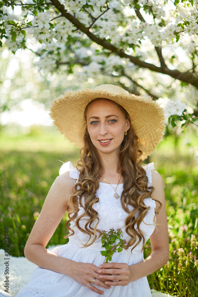 Fototapeta premium The beautiful girl the blonde in the blossoming apple-trees garden. White flowers in a garden in sunshine. Spring apple trees in blossom. Beautiful woman among spring blossom