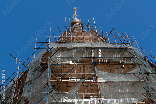closeup photo of renovation of white christian chirch with scaffolding around on blue sky background