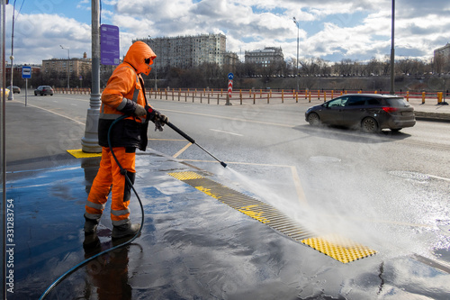 Road worker cleaning city street with high pressure power washer, cleaning dirty public transport stops, Moscow, Russia photo