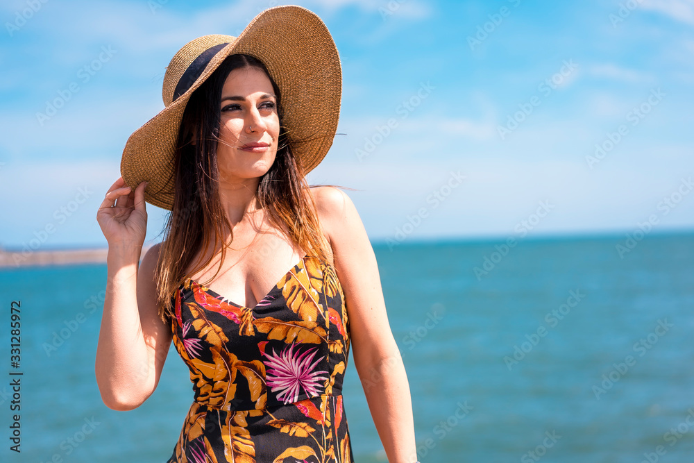Lifestyle, portrait of a smiling brunette girl in hat and floral dress