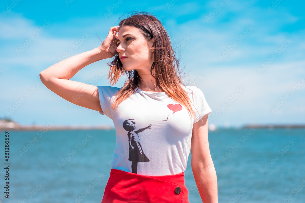 Lifestyle, a dreamy brunette looking left in a white t-shirt, a red short skirt by the sea Lifestyle, a dreamy brunette looking left in a white t-shirt, a red short skirt by the sea