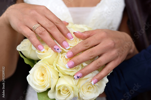 Hands of the bride with ring on a bouquet of white roses
