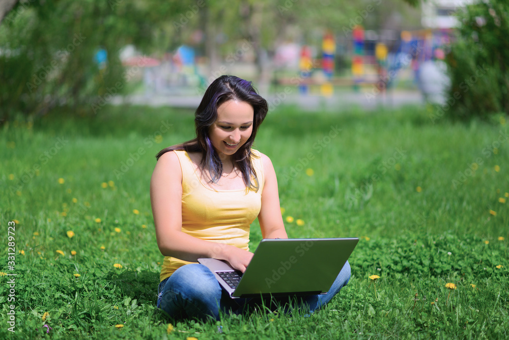 a girl with a laptop sitting in a city Park on the lawn on a hot summer day