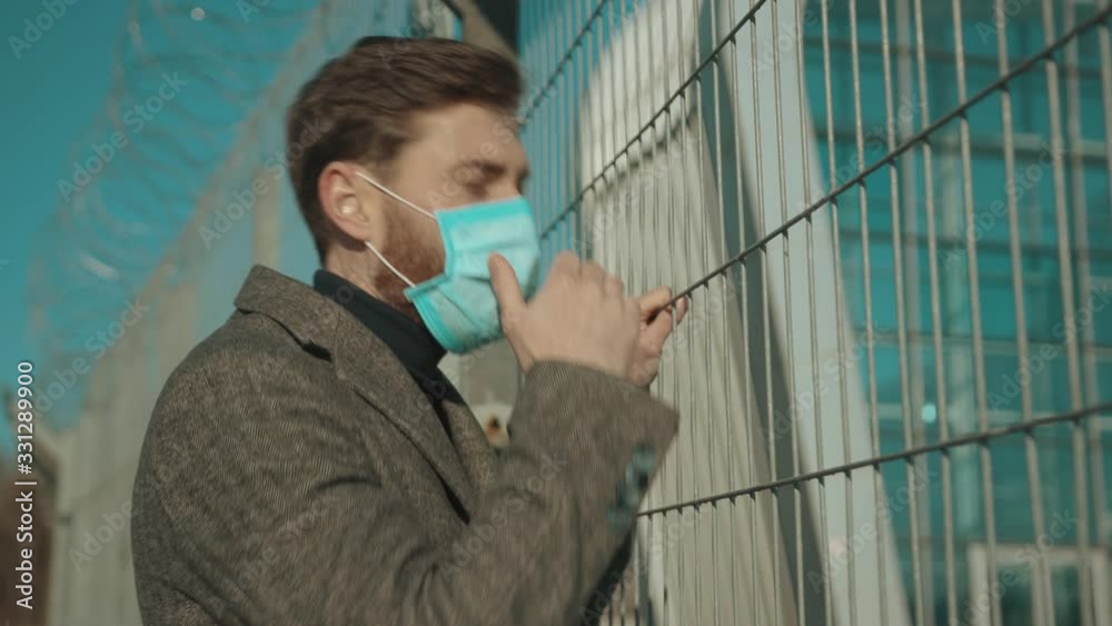Face man wearing Protective Face Mask stand near fence border COVID-19 coronavirus infection pandemic disease virus male tourist epidemic air health illness slow motion