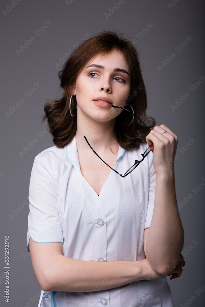 An attractive Italian doctor in a white coat looks thoughtfully away and puts glasses to her mouth. An attractive Italian doctor in a white coat looks thoughtfully away and puts glasses to her mouth.