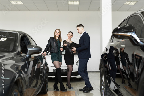 Auto business, car sales - a couple of friends of girls with a car dealer choose a car in a car dealership