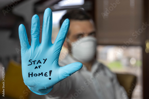 Young man with an open palm with a glove and a mask on which is written stay at home, quarantine concept coronavirus