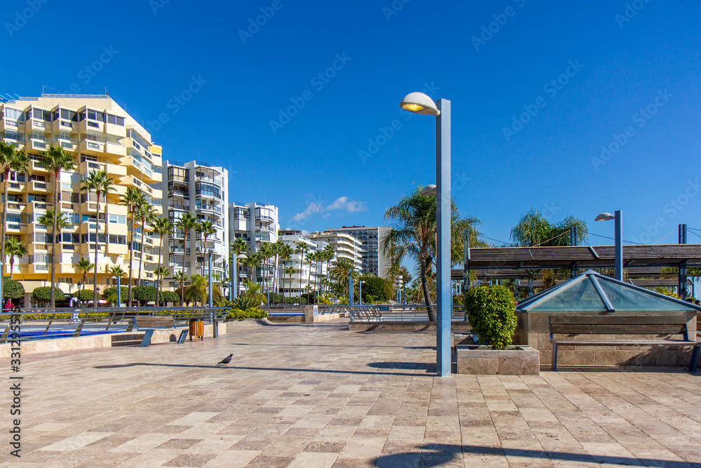 Marbella city promenade area near the city bay. Empty square. In background Marbella beachfront homes, luxury and expensive real estate. Palm tree, blue sky Marbella city promenade area near the city bay. Empty square. In background Marbella beachfront homes, luxury and expensive real estate. Palm tree, blue sky