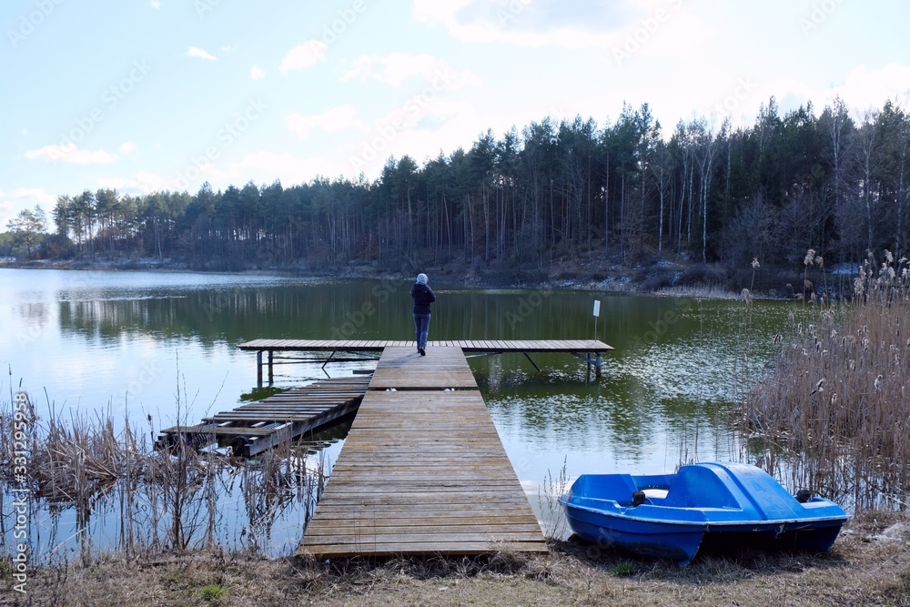 Silhouette of lonely woman standing on jetty at the Gogolinek Lake in Bory Tucholskie. A boat lying on the shore next to the rushes. Poland