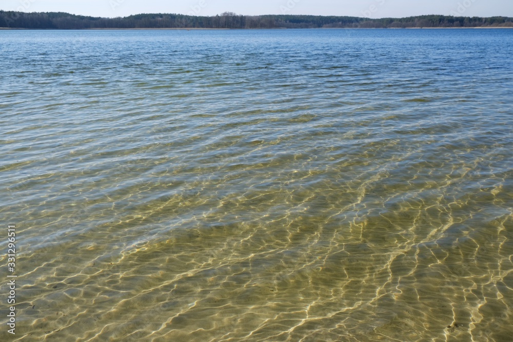 Transparent water in the lake - visible bottom with white sand and light reflections Transparent water in the lake - visible bottom with white sand and light reflections