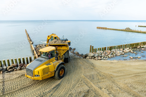 an excavator on the beach loads sand and stones into the truck body  works to strengthen the beach and install breakwaters
