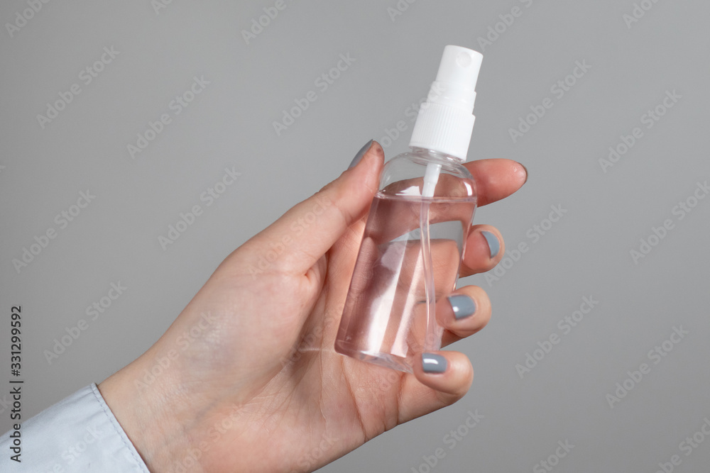 Female hand holds a plastic bottle with a sanitizer spray on a gray background removed. A tool for protection against coronavirus, pandemic Female hand holds a plastic bottle with a sanitizer spray on a gray background removed. A tool for protection against coronavirus, pandemic