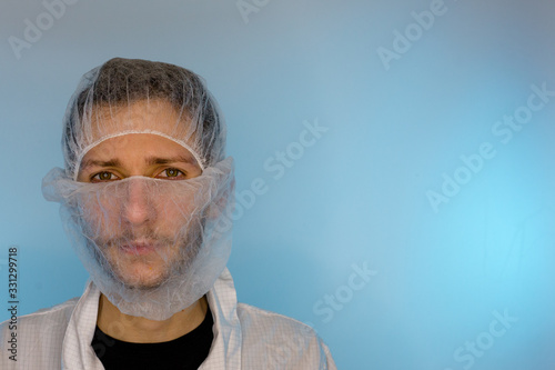 An adult male dressed in a white lab coat with a hair net and beard net on. Ready to work in a clean room or laboratory