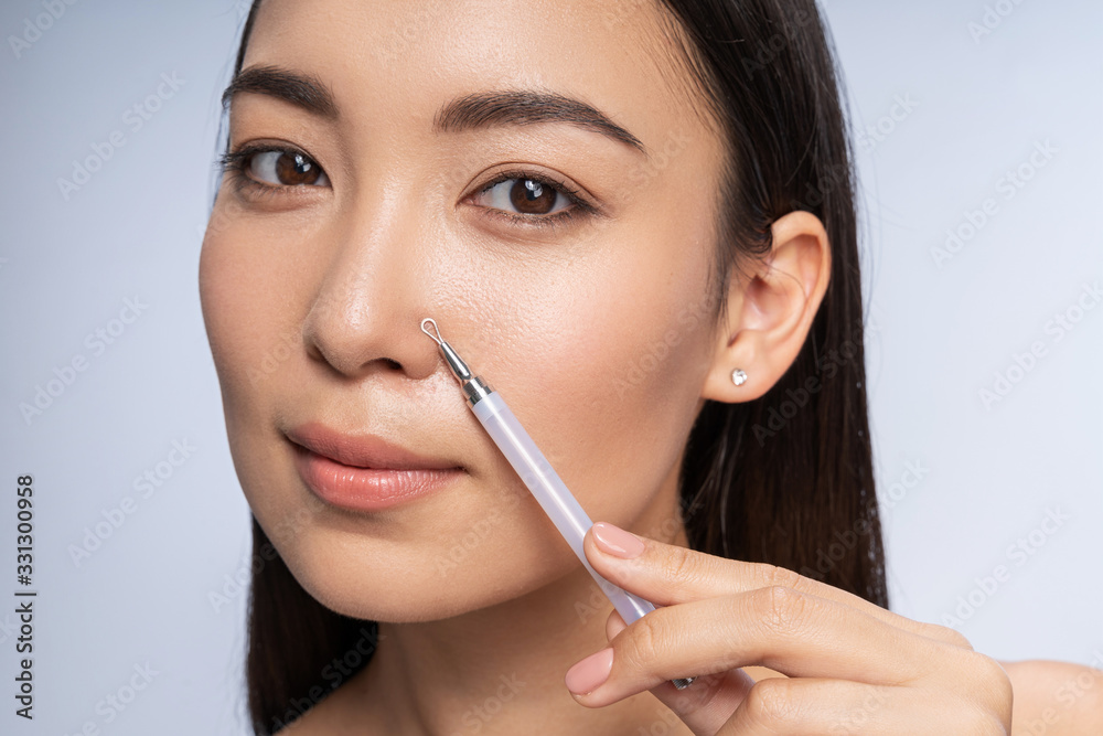 Pretty Asian woman is squeezing acne indoors Pretty Asian woman is squeezing acne indoors