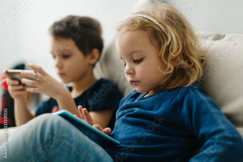 2 children a boy and a girl sit on gadgets and play phones in the afternoon