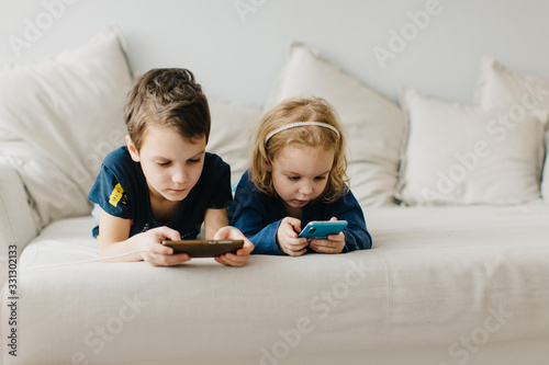 2 children a boy and a girl sit on gadgets and play phones in the afternoon