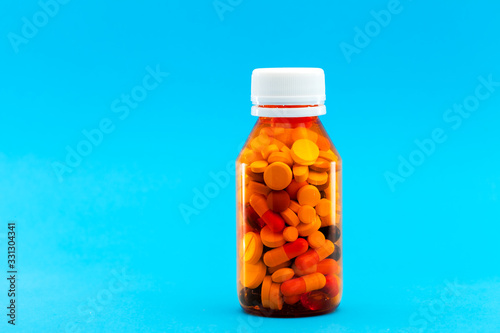 orange transparent bottle for medicines filled with different pills, concept on a medical theme on a blue background with copy space.