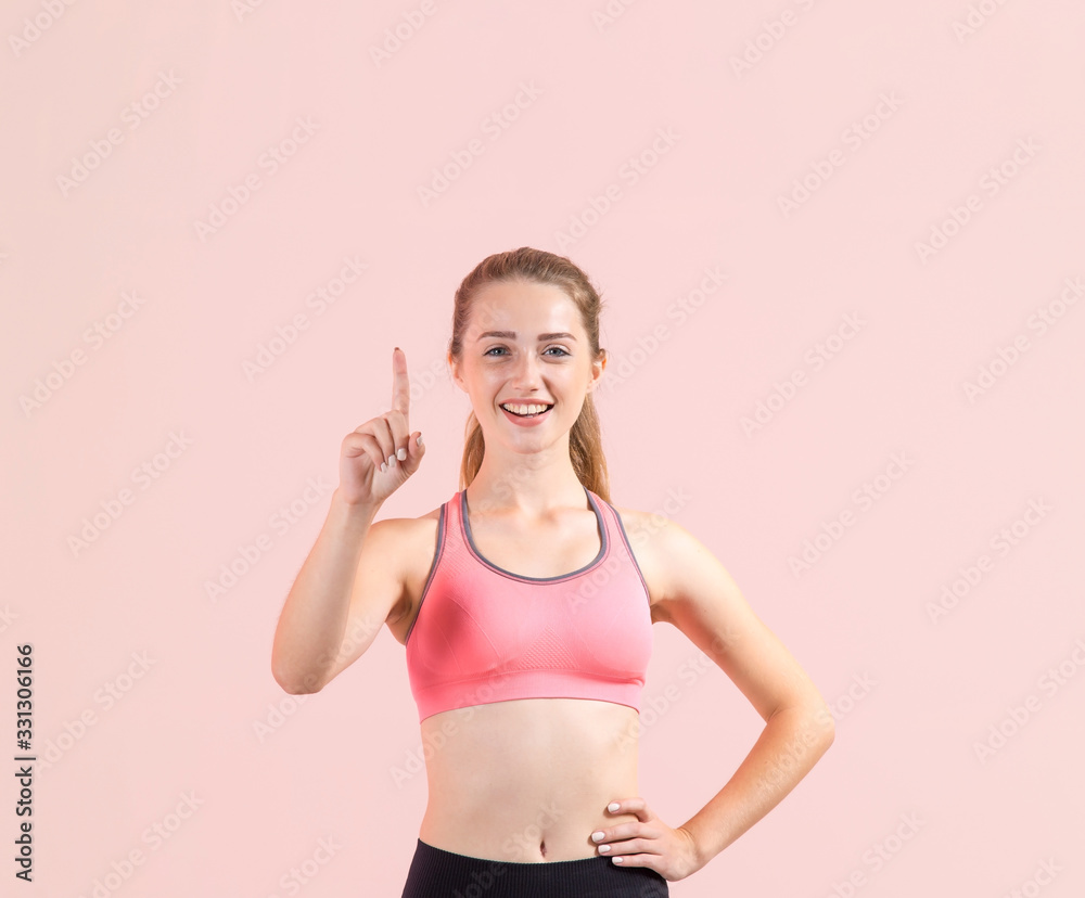 Young fitness woman points a finger in upward standing on a light pink background. Sportswoman pointing up on copy space and looking at the camera.