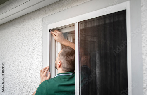 freundlicher Handwerker montiert Insektenschutzgitter bei einem Kunden zu Hause