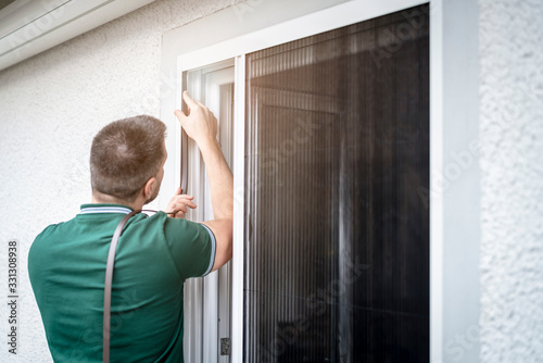 freundlicher Handwerker montiert Insektenschutzgitter bei einem Kunden zu Hause