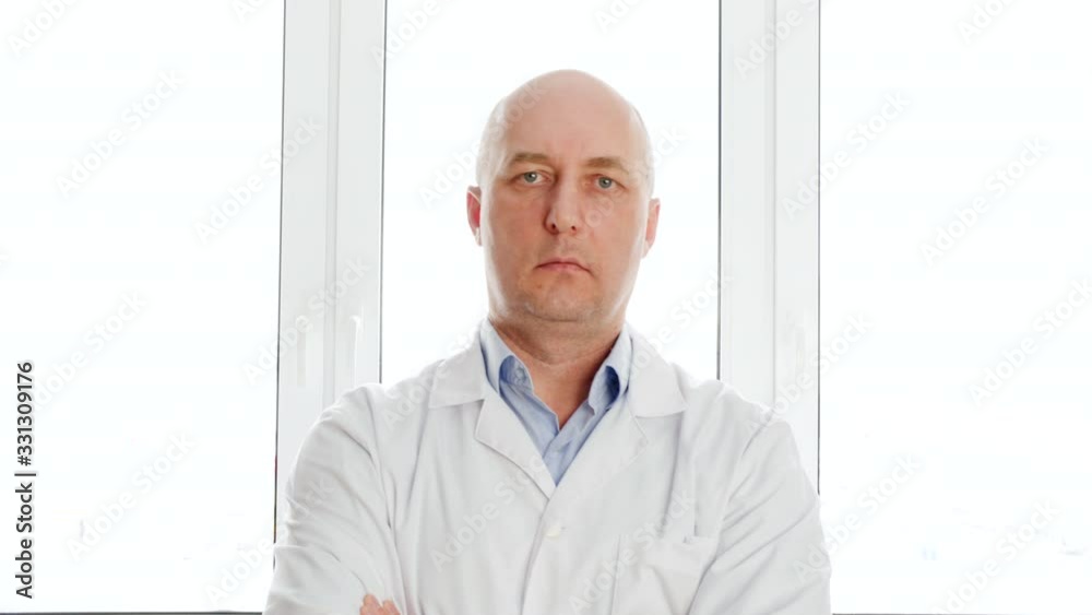 Confident engineer with crossed arms posing near window. Serious male medical worker standing near window. Confidence concept Confident engineer with crossed arms posing near window. Serious male medical worker standing near window. Confidence concept
