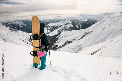Female hiker with snowboard and walking sticks on mountain top