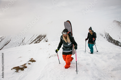 Two travellers with snowboards climbing on mountain
