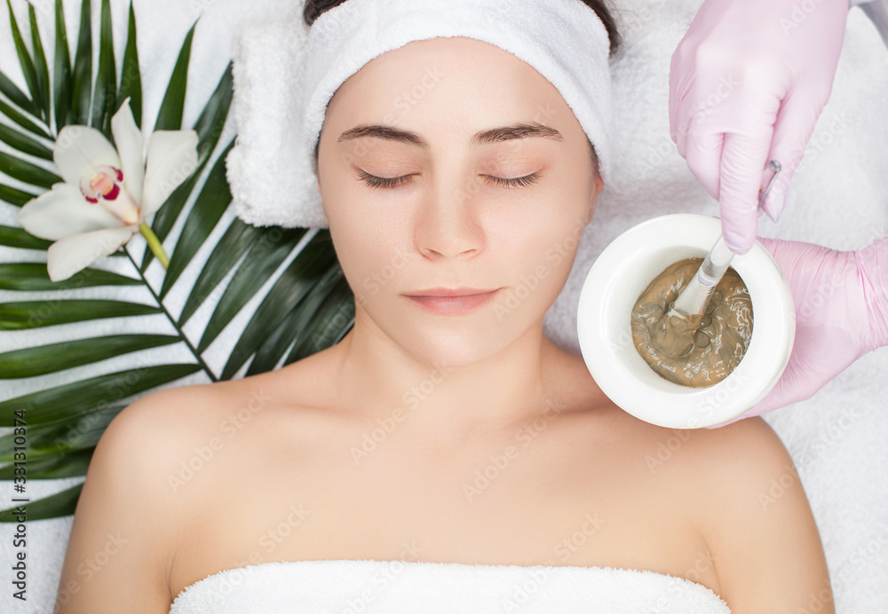 Φωτογραφία Beautician makes a face clay mask against acne on the face of a woman to rejuvenate the skin