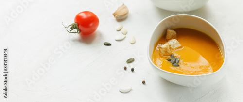 Pumpkin soup in a white porcelain bowl on a white background with cherry tomatoes and seeds, with space