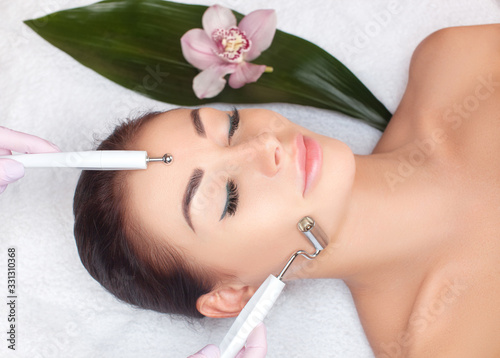 The cosmetologist makes the apparatus procedure of Microcurrent therapy for a beautiful, young woman in a beauty salon. Cosmetology and professional skin care. photo