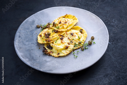 Traditional Italian ravioli pasta offered with capers and onion chili pesto closeup on a modern design plate
