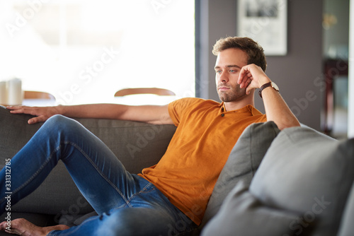 Young man sitting on his sofa deep in thought