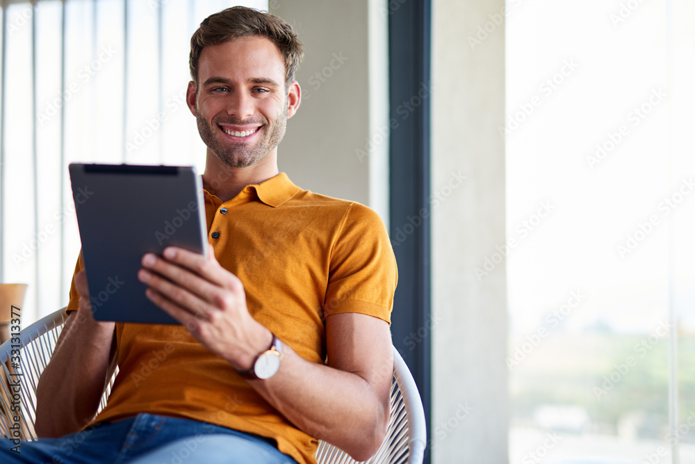 Smiling young man sitting at home using a tablet Smiling young man sitting at home using a tablet
