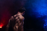 Muscular man showing muscles isolated on the black background with colored smoke. Concept of healthy lifestyle 