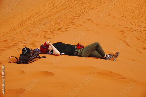 A woman (tourist) lies on sand | has rest under the sun. Backpack and camera lie by. Wadi Rum desert, Jordan.