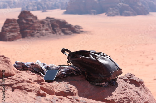 Traveller's stuff (leather backpack, shirt, phone on a high rock above a rocky desert. Wadi Rum, Jordan © Natalia