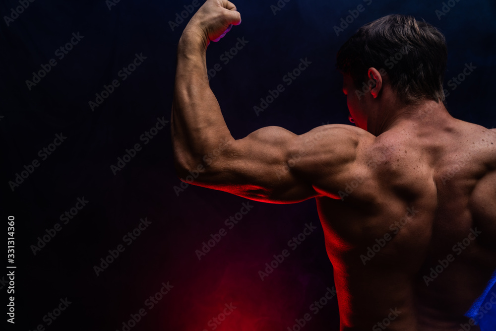 Muscular man showing muscles isolated on the black background with colored smoke. Concept of healthy lifestyle Muscular man showing muscles isolated on the black background with colored smoke. Concept of healthy lifestyle