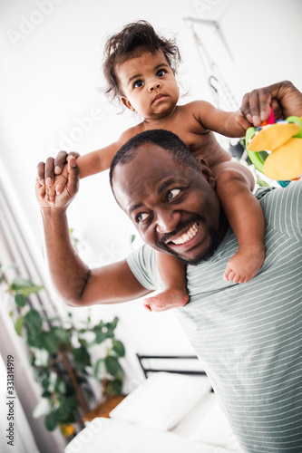 Joyful Afro American man carrying baby girl on his shoulders