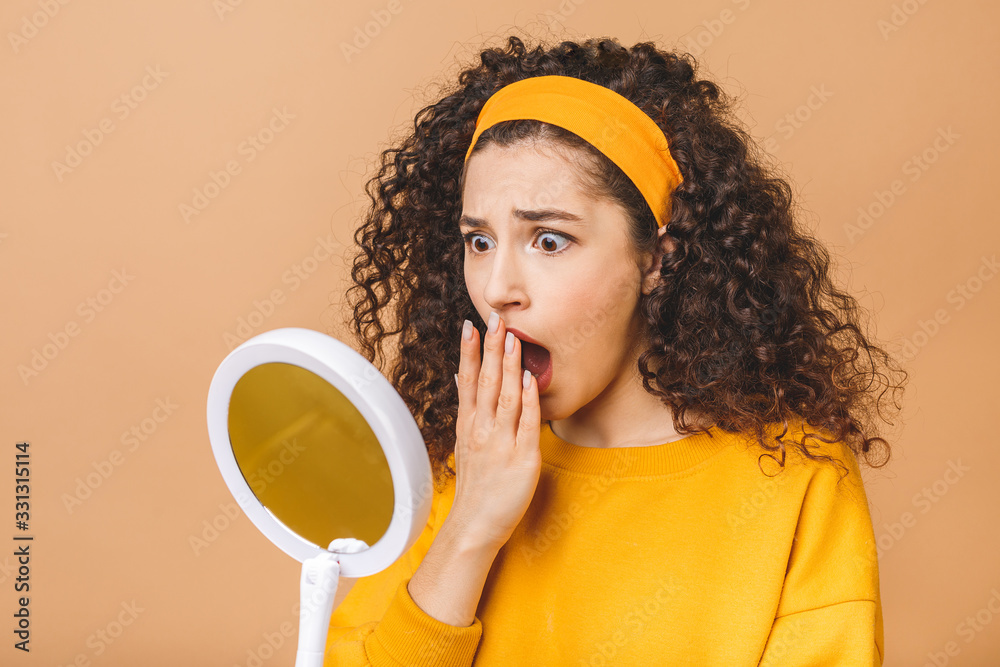 Φωτογραφία Beauty portrait of an astonished shocked amazed attractive curly woman examining her face while holding a mirror isolated over beige background