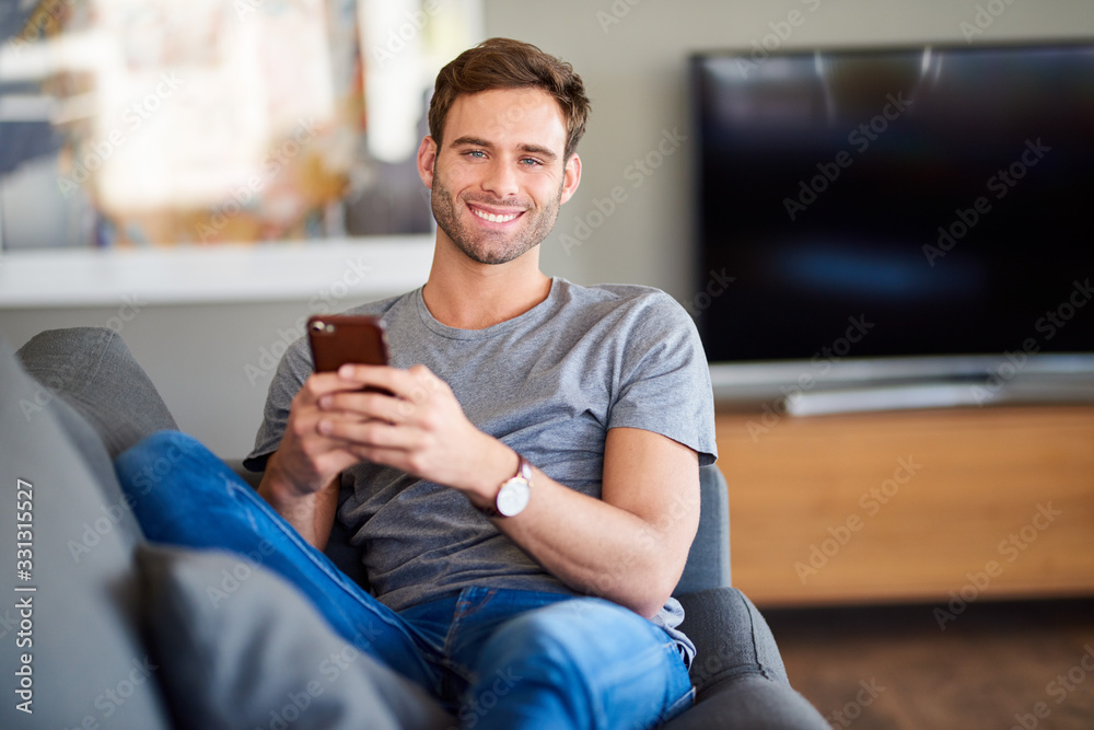 Smiling young man using a cellphone on his sofa