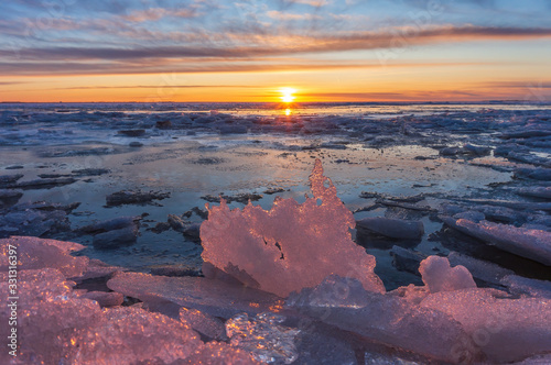 winter or spring sunset against the backdrop of a semi-frozen bay with pieces of ice and pink ice floes in the sun