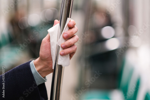 Close up of man hand holds a handrail in public transport/subway through a napkin, to protect yourself from contact with viruses, germs during a coronavirus pandemic, covid-19. Quarantine concept