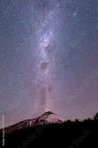 Thousands of stars in the sky with the Milky Way above the Villarrica Volcano in Chile with silhouettes of some trees  vertical photo