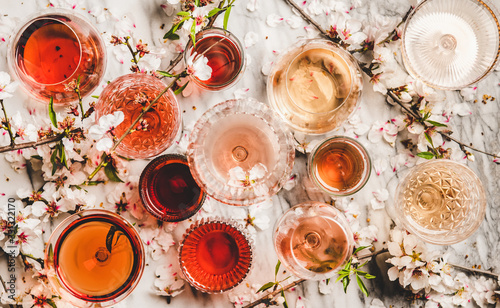 Various shades of rose wine. Flat-lay of rose wine in different colors in glasses and spring blossom flowers over marble background, top view. Wine shop, bar, tasting, seasonal wine list concept